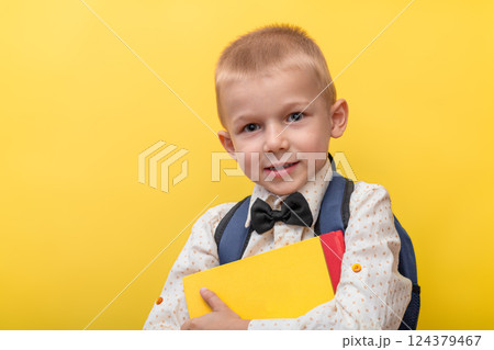 Back to school. A blond funny boy with a backpack in a light shirt on a yellow background holds books in his hands and looks at the camera. 124379467