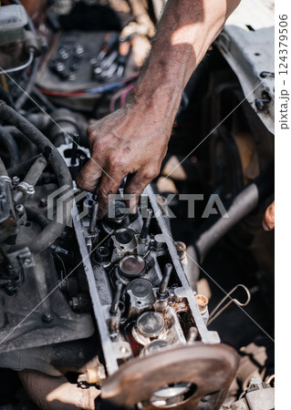 A worker repairs the cylinder head of an automobile engine. Oil removal valve. Car repairs. Car service A worker repairs the cylinder head of an automobile engine. Oil removal valve. Car repairs. Car service 124379506