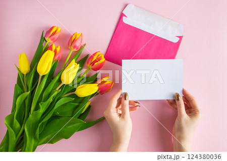 Woman holds greeting card in her hands. Gift for spring holiday. Bouquet of fresh tulips on pink background. Woman holds greeting card in her hands. Gift for spring holiday. Bouquet of fresh tulips on pink background. 124380036
