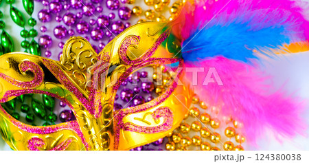 Golden carnival mask and colorful beads close-up. Mardi Gras or Fat Tuesday symbol. Concept of traditional festival. Holiday decorations in gold, green and purple. Golden carnival mask and colorful beads close-up. Mardi Gras or Fat Tuesday symbol. Concept of traditional festival. Holiday decorations in gold, green and purple. 124380038