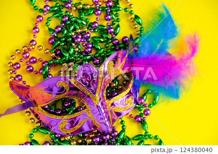 Carnival mask and beads on yellow background. Mardi Gras concept. Fat Tuesday symbol. Holiday decorations close up. 124380040