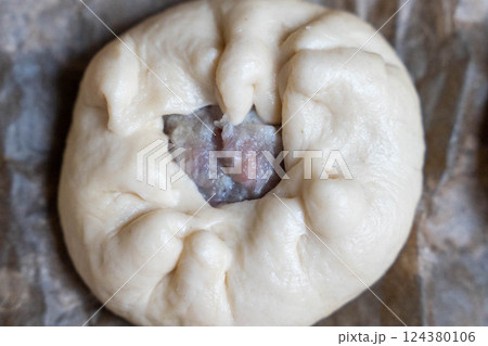 Raw baozi bun showing filling on baking paper: preparation in kitchen 124380106