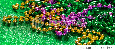 Mardi Gras concept. Multi-colored beads on green shiny background. Fat Tuesday symbol. Festive shining decorations in gold, green and purple colors for traditional holiday. Banner format. Mardi Gras concept. Multi-colored beads on green shiny background. Fat Tuesday symbol. Festive shining decorations in gold, green and purple colors for traditional holiday. Banner format. 124380167