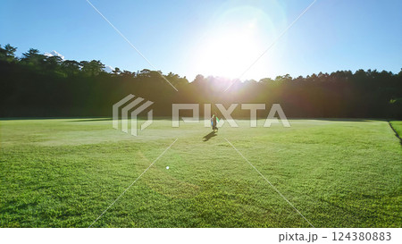 太陽の日差しをバックに一面に広がる木々の林の下の広大な芝生の上をゆっくりと歩く一人の女性 124380883