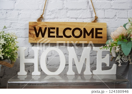 Welcome Home alphabet letters and wooden signboard hanging on white brick wall background 124380946