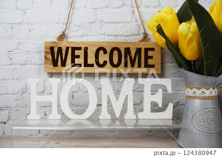 Welcome Home alphabet letters and wooden signboard hanging on white brick wall background 124380947