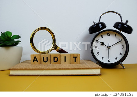 Magnifying glass and alarm clock with wooden blocks alphabet letters AUDIT text message on yellow background Magnifying glass and alarm clock with wooden blocks alphabet letters AUDIT text message on yellow background 124381155