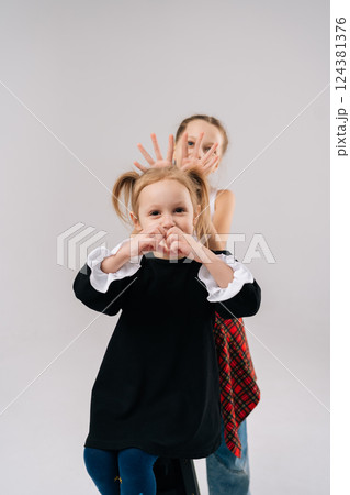 Playful young sisters posing together, sharing lighthearted moments in professional studio setting with white isolated background, expressing joyful connection through animated facial expressions. 124381376