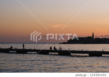People on a pier at sunset by the Mediterranean Sea, silhouettes, old town in the background. People on a pier at sunset by the Mediterranean Sea, silhouettes, old town in the background. 124381410