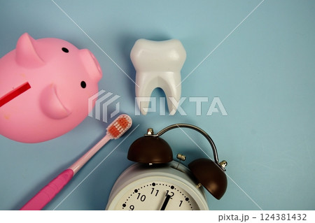 White tooth model with toothbrus, alarm clock and piggy bank on blue background, dental hygiene concept White tooth model with toothbrus, alarm clock and piggy bank on blue background, dental hygiene concept 124381432