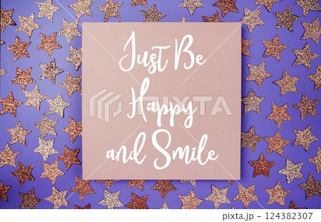 Just Be Happy and Smile text  motivational and inspiration quote on paper card with star glitter decoration flat lay on purple background 124382307