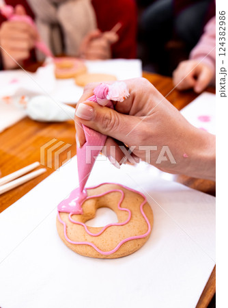 Female decorating pink icing cookie with piping bag at baking class Female decorating pink icing cookie with piping bag at baking class 124382986