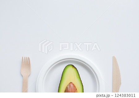 Minimalistic half avocado on white plate with wooden cutlery 124383011