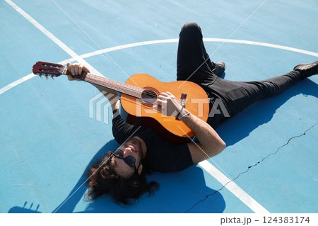 Man Lying On The Ground Plays Classical Guitar On Blue Floor Outdoor 124383174