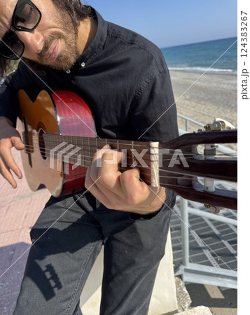 Long Hair Boy Plays Classical Guitar by the Ocean in Summer Dressed in Black 124383267