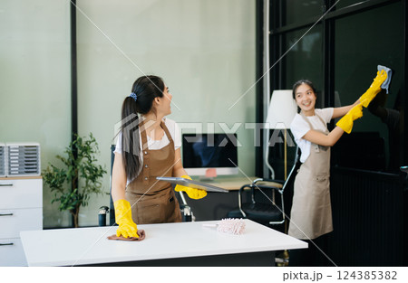 Two professional cleaners tidying a stylish space with a smile. Experience efficient and friendly house cleaning Two professional cleaners tidying a stylish space with a smile. Experience efficient and friendly house cleaning 124385382