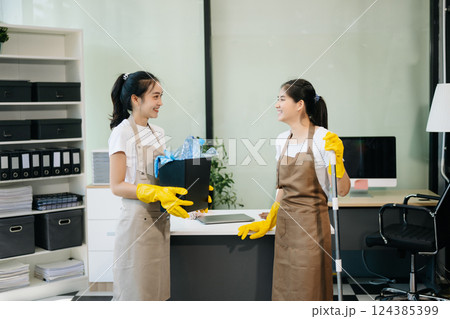 Two professional cleaners tidying a stylish space with a smile. Experience efficient and friendly house cleaning Two professional cleaners tidying a stylish space with a smile. Experience efficient and friendly house cleaning 124385399