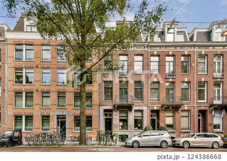 Brightly colored traditional buildings line a serene street, showcasing the unique architectural style of Amsterdam, complemented by bicycles and parked cars. 124386668