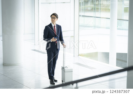 スマートフォンとキャリーケースを持った40代のビジネスマン スマートフォンとキャリーケースを持った40代のビジネスマン 124387307