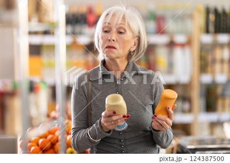 Elderly woman chooses mustard or mayonnaise sauces 124387500