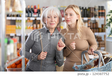 Elderly mother with her adult daughter choose and buy groceries together in the grocery department of supermarket Elderly mother with her adult daughter choose and buy groceries together in the grocery department of supermarket 124387752