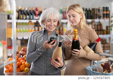 Elderly mother and her adult daughter scan a QR code on a bottle of wine label together to check expiration date Elderly mother and her adult daughter scan a QR code on a bottle of wine label together to check expiration date 124387805