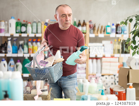Man with basket of goods looks at display case, looks for household chemistry items Man with basket of goods looks at display case, looks for household chemistry items 124387819