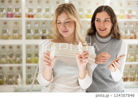 Girl offers her friend to check quality of perfume by scanning QR code with smartphone 124387846