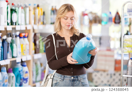 Girl housewife in household store examines goods, chooses liquid detergent Girl housewife in household store examines goods, chooses liquid detergent 124388045
