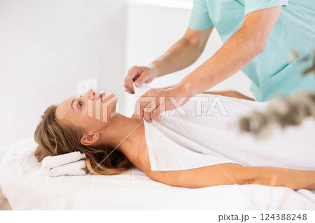 Relaxed middle-aged woman lying on massage table covered with blanket by masseuse 124388248