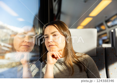Reflective woman looking through train window while journeying 124388346