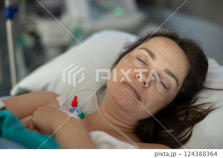Female patient, connected to IV, sleeping in hospital bed after surgery 124388364