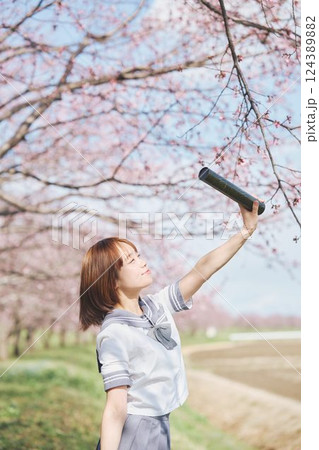 青空と桜の下の卒業少女を持つ女子高生 124389882