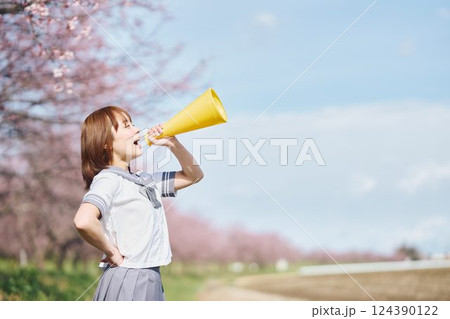 桜の下メガホンで応援する女子高生 124390122