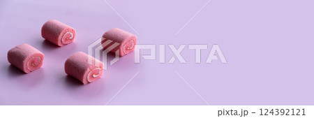 Four pink cupcakes resembling rolled pastries are arranged on a soft rose-patterned surface. 124392121
