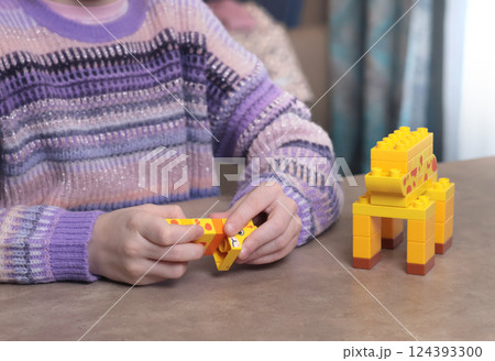 Girl plays with constructor at home on table. African animals. Children and educational games. Girl plays with constructor at home on table. African animals. Children and educational games. 124393300