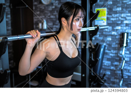 パワーラックマシンのバーベルを背負う、ジムで体を鍛えるかっこいい女性　筋トレ女子　 124394803