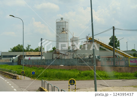 Manufacturing facility with towering silos and conveyor belts under a bright sky in a bustling industrial area 124395437