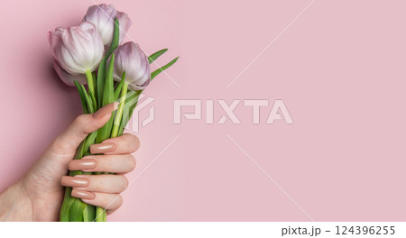 Woman hand holding beautiful pink tulips showing manicure nails on pink background 124396255