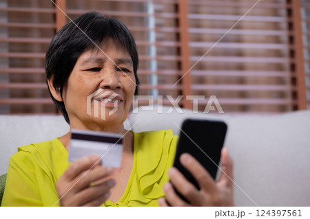 Senior asian woman sitting on sofa using smart phone shopping online with credit card buying. Senior asian woman sitting on sofa using smart phone shopping online with credit card buying. 124397561