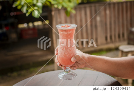Hands showing strawberry smoothie on wooden table. People hand holding a strawberry milkshake on wood, Hands holding strawberry smoothie on wooden table with blurred background 124399414