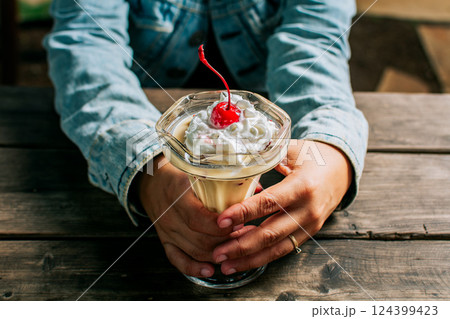Female hand holding cherry milkshake on wooden table. Person holding cherry smoothie over wooden table| Female hand holding cherry milkshake on wooden table. Person holding cherry smoothie over wooden table| 124399423