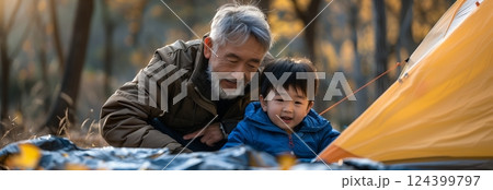 A heartwarming moment between a grandfather and grandson while camping in the serene outdoors, enjoying nature together. 124399797