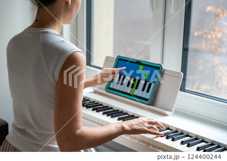 Young woman learning to play the keyboard at home using an interactive app. Using mobile apps for self-study concept Young woman learning to play the keyboard at home using an interactive app. Using mobile apps for self-study concept 124400244