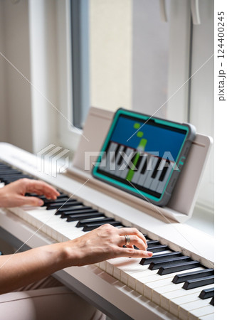 Hands playing a keyboard while following an interactive learning app on a tablet. Technology enables self-education in music without traditional lessons. Hands playing a keyboard while following an interactive learning app on a tablet. Technology enables self-education in music without traditional lessons. 124400245