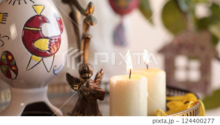 Celebrate Easter with handcrafted Easter decorations featuring a colorful egg, an angel figurine, and lit candles in a cozy setting Celebrate Easter with handcrafted Easter decorations featuring a colorful egg, an angel figurine, and lit candles in a cozy setting 124400277