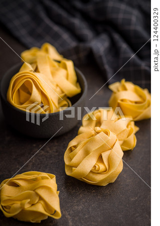 Italian pasta tagliatelle. Uncooked noodle pasta on black table. Italian pasta tagliatelle. Uncooked noodle pasta on black table. 124400329