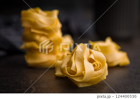 Italian pasta tagliatelle. Uncooked noodle pasta on black table. Italian pasta tagliatelle. Uncooked noodle pasta on black table. 124400330