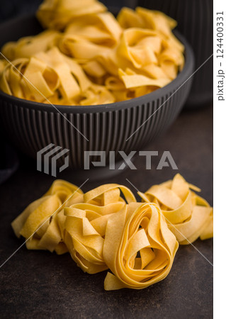 Italian pasta tagliatelle. Uncooked noodle pasta on black table. 124400331