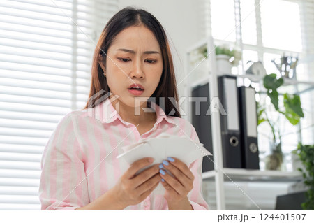 Financial Stress and Home Office Challenges. A woman with a worried expression examining her bills in her workspace. 124401507